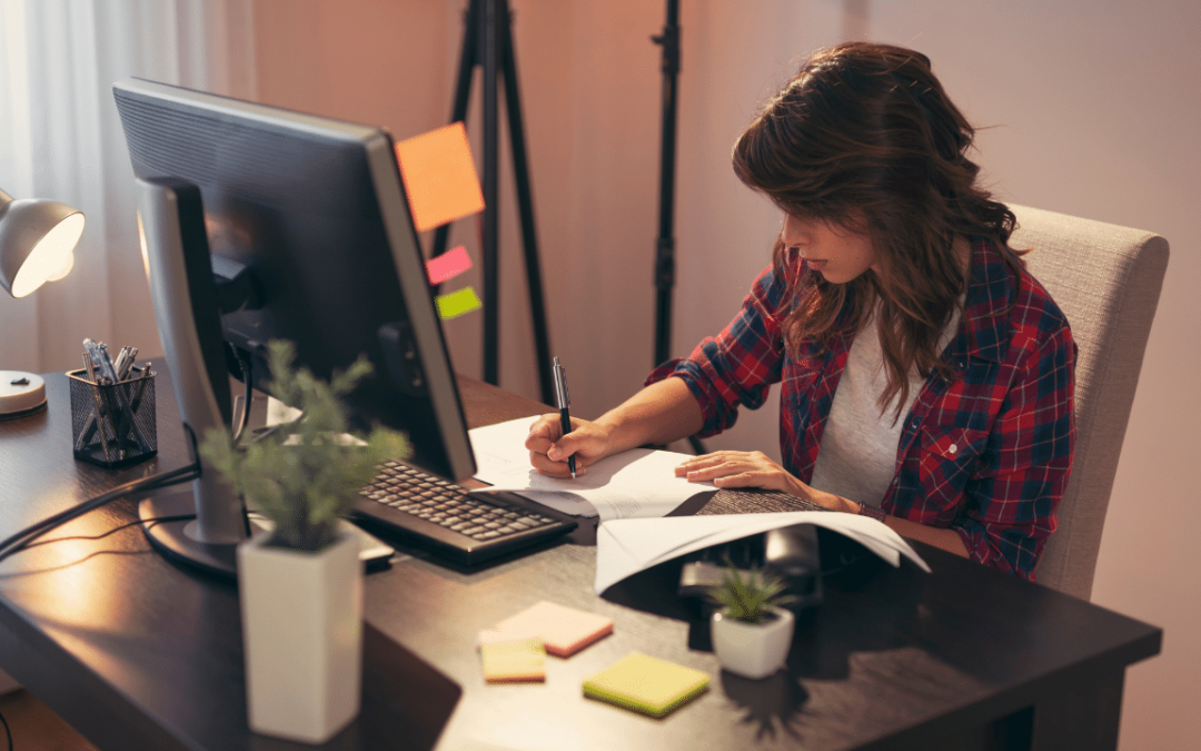 Woman sitting at home office desk writing on a piece of paper