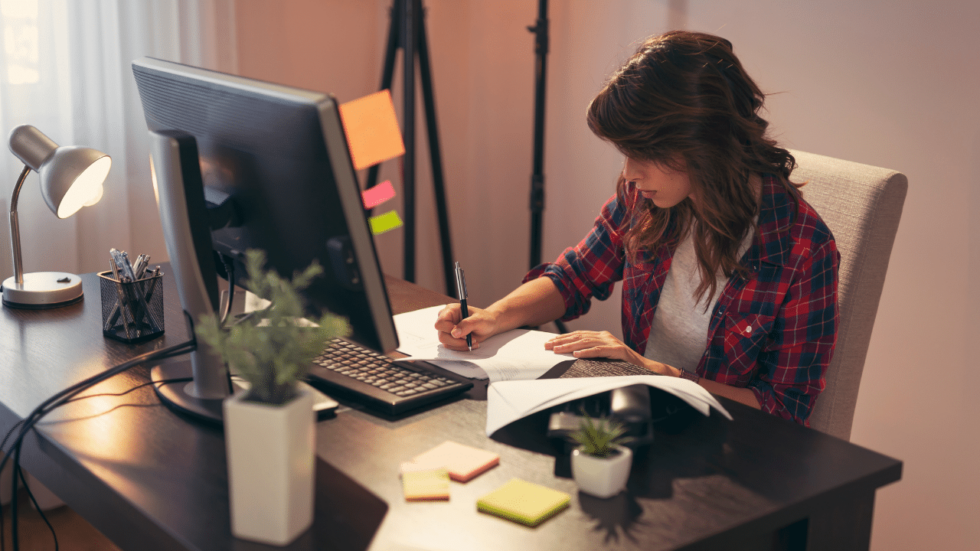 Woman sitting at home office desk writing on a piece of paper