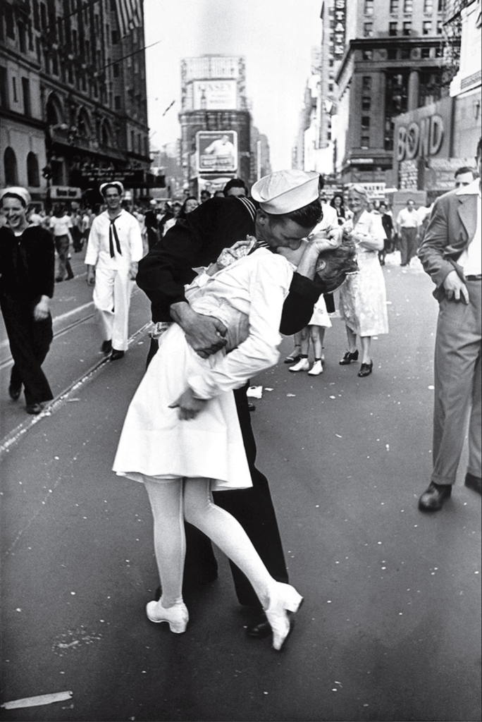In New York’s Times Square a white-clad girl clutches her purse and skirt as an uninhibited sailor plants his lips squarely on hers