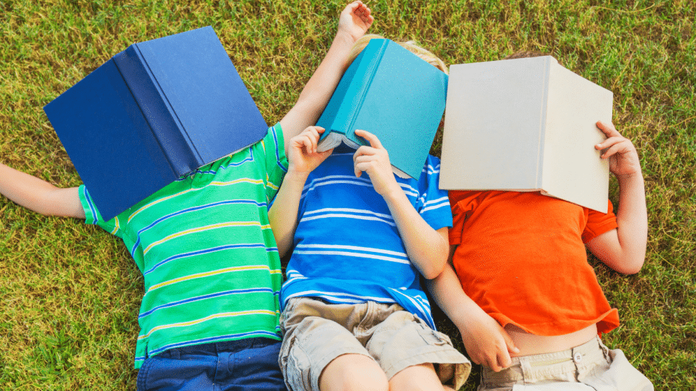 Three children laying in the grass with books