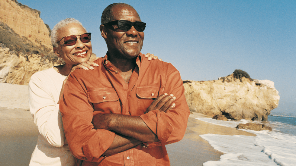 Two retired military members on a beach smiling