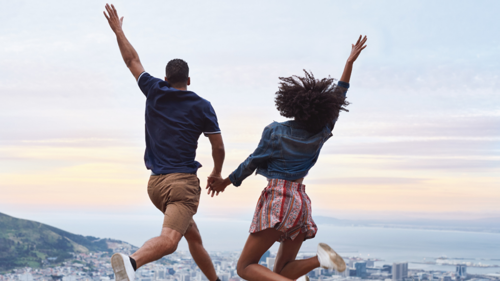 Couple holding hands, jumping as the sun sets over San Diego.