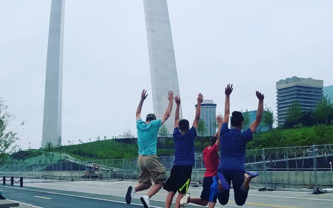 Family jumping excitedly in front of the St. Louis Arch