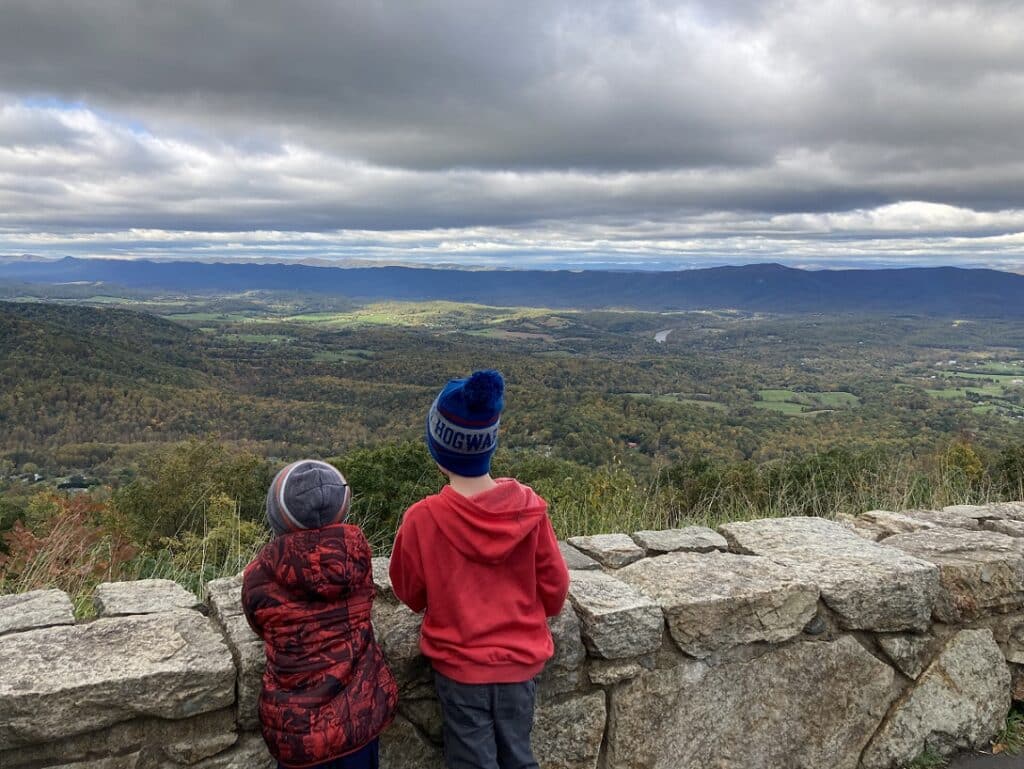 Two children looking out over a valley while dark grey clouds are overhead