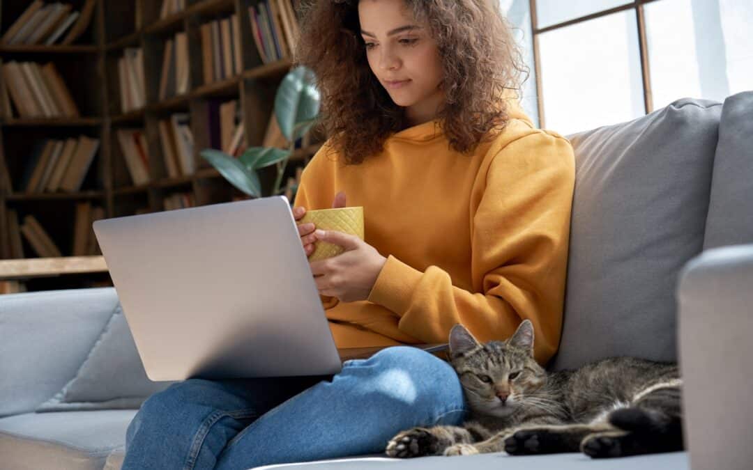 Woman sitting on the couch with her cat and laptop, drinking a coffee